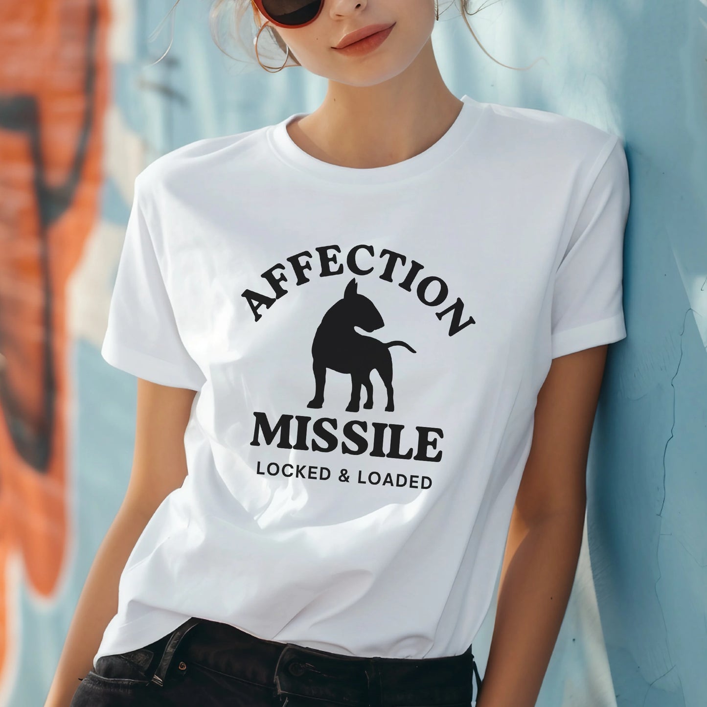 Person wearing a white t-shirt with a graphic design and text "Affection Missile Locked & Loaded" against a graffiti-covered wall.