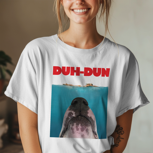 Person wearing a white t-shirt with a parody graphic inspired by the JAWS movie poster of a dog's face and 'DUH-DUN' text