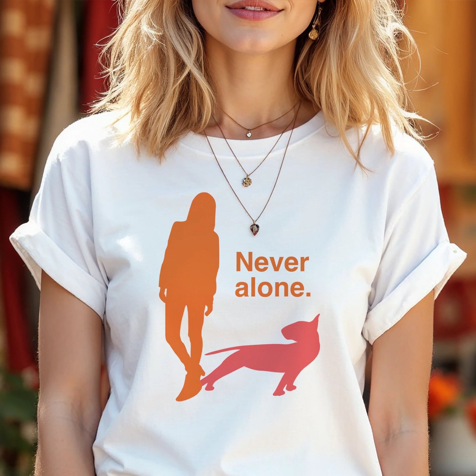 Person wearing a white t-shirt with a graphic of an orange figure and coral bull terrier shadow, and the text 'Never alone.' 