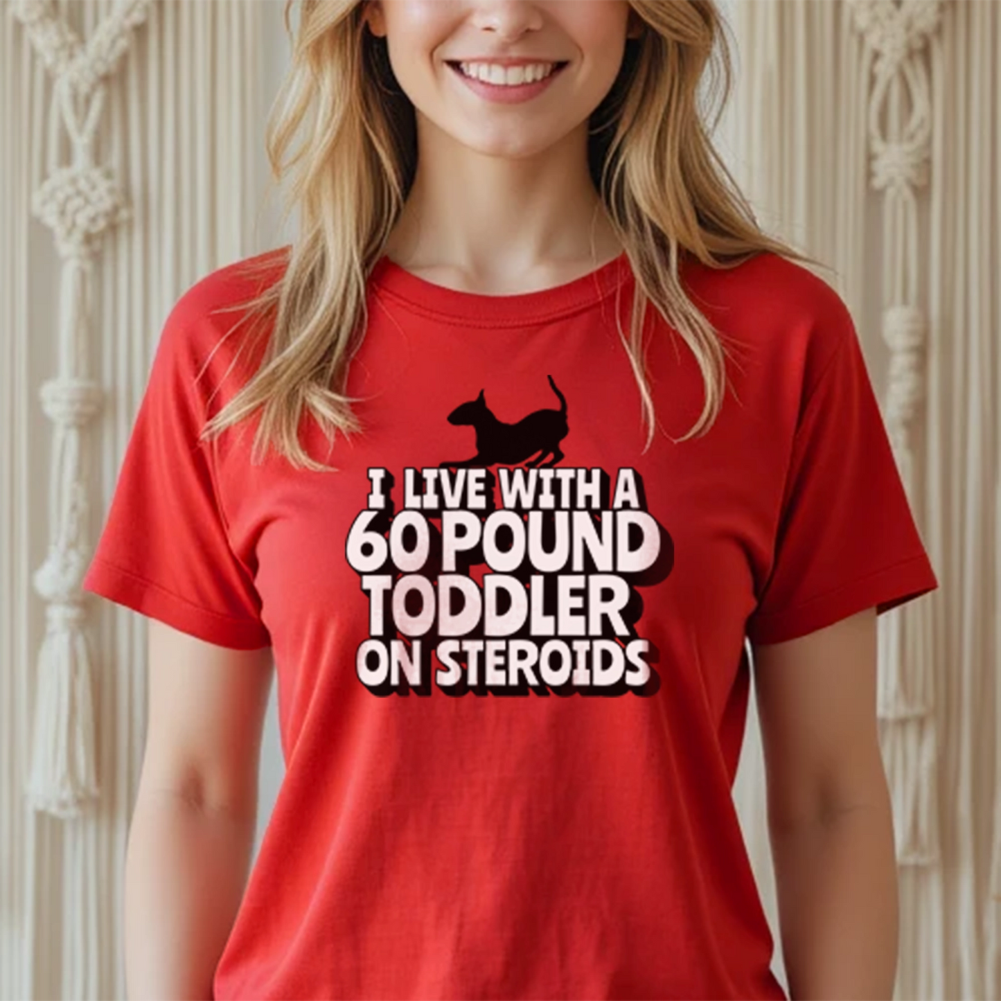Person wearing a red t-shirt with a graphic of a bull terrier and text "I' Live with a 60-Pound toddler on steroids"