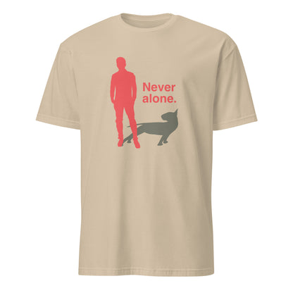 Product mockup of a sand t-shirt with a graphic of a red figure and grey bull terrier shadow, and the text 'Never alone.' on a city street.